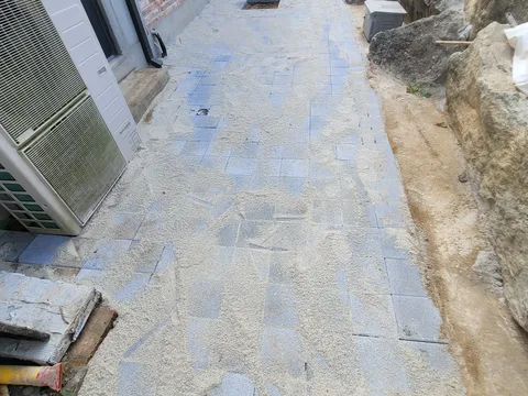상가 건물 옆 좁은 통로에 화강석 판석을 깔고 물걸레질 자국과 줄눈 시멘트 가루가 남은 마감 단계