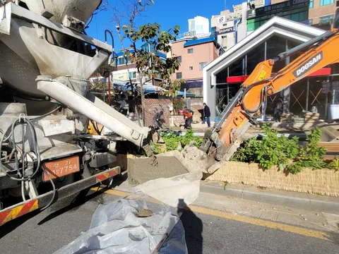 레미콘 차량과 굴착기가 도심 상가 앞 인도에서 콘크리트를 붓거나 걷어내는 철거·타설 작업