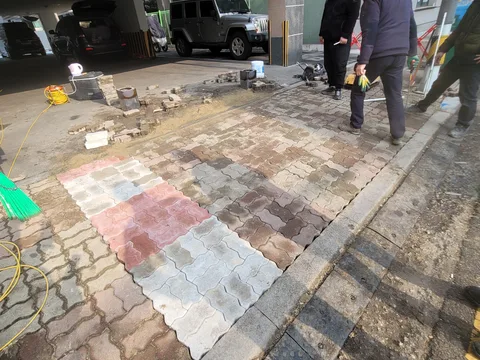 도로변 보도에 회색·붉은색·베이지색 물결무늬 인터로킹 블록을 색상별로 배열해 패턴을 만드는 시공 장면