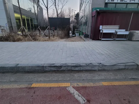 상가 매장 앞 보도블럭 경계석이 갈라지고 들뜬 채 주황 도색 차선과 맞닿은 모습