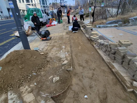 도로변 화단 옆 보도에서 여러 작업자가 모래바닥을 다지며 정리하는 모습