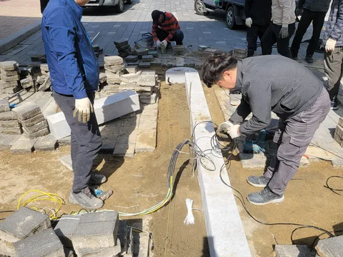 새로 놓은 흰색 경계석 라인을 다수의 작업자가 정리하며 단차가 있는 구간을 다듬는 모습