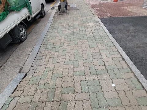 트럭이 주차된 도로변 인도에 연두빛 톤의 물결무늬 인터로킹 블록을 완료 상태로 포장한 구간