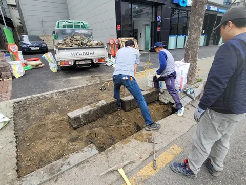 트럭에서 경계석 자재를 내려 도로변에 새로 설치 중인 여러 작업자